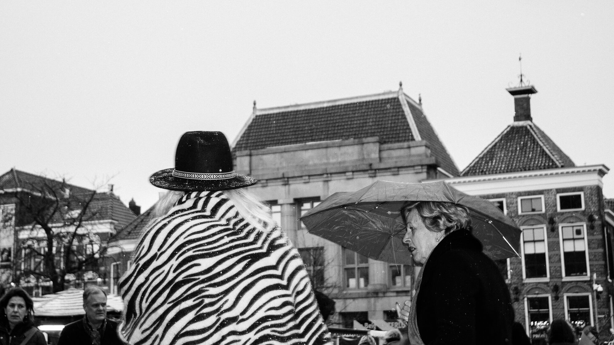 Vrouw met hoed en een vrouw met paraplu trotseren een winters bui in de stad Groningen.