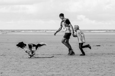 Berenloper samen met hond en kind op het strand.