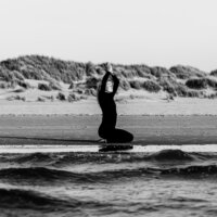Ezra Goudzwaard van Yogiez Yoga doet een zittende zonnegroet bij het water