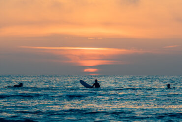 Drie surfers bewonderen een zonsondergang bij Formerum aan Zee