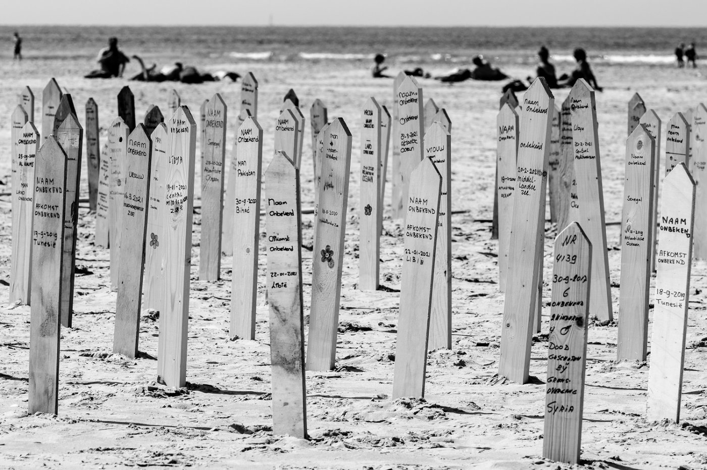 Herdenkingsborden met op de achtergrond toeristen op het strand bij West aan Zee
