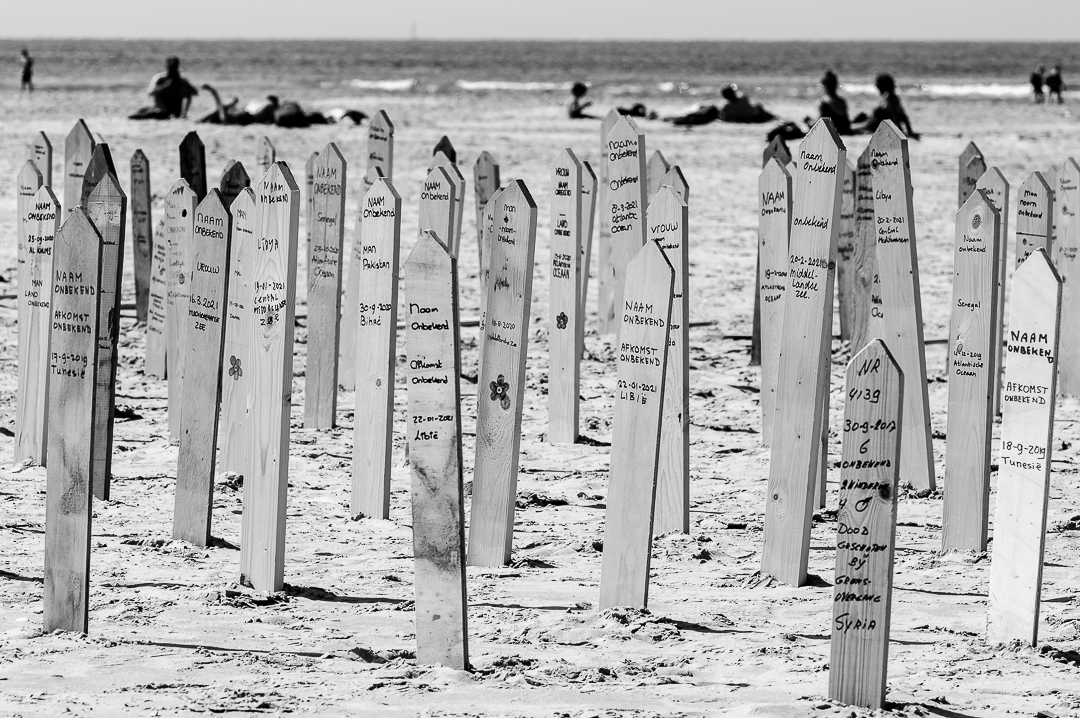 Herdenkingsborden met op de achtergrond toeristen op het strand