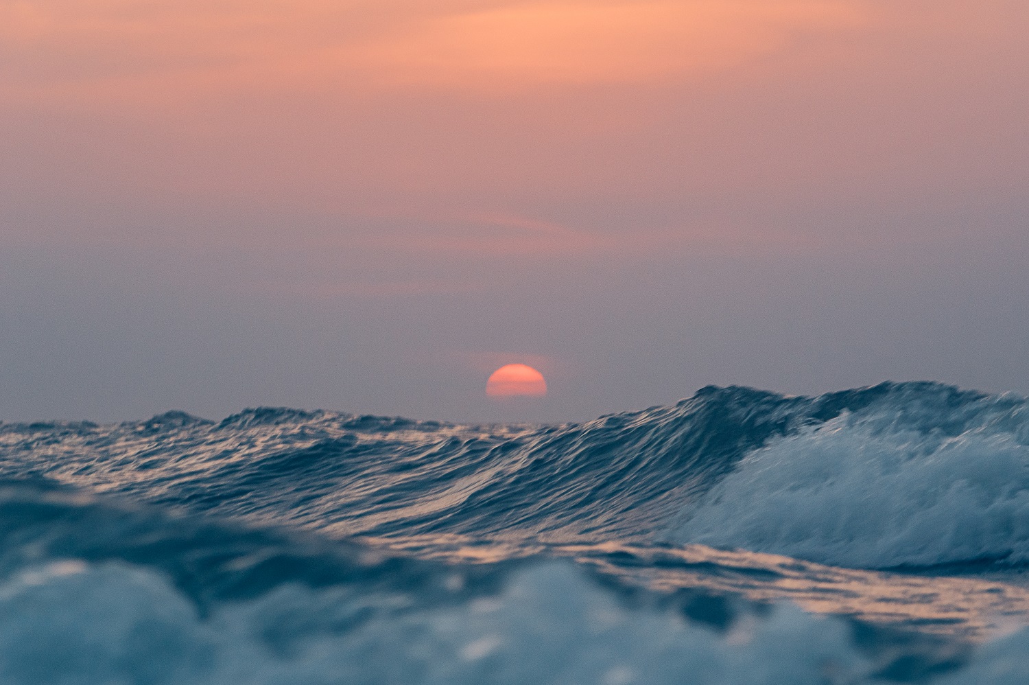Rode ondergaande zon vlak boven de blauwe golven van de Noordzee