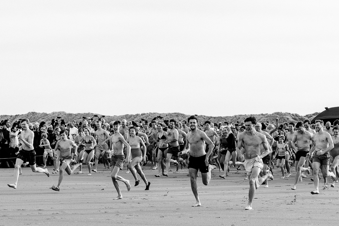 Grote groep deelnemers sprint naar de zee